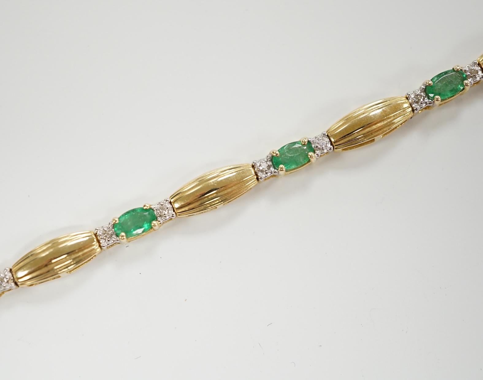 A modern yellow metal, emerald and diamond chip cluster set bracelet, 17.7cm, gross weight 7.6 grams.